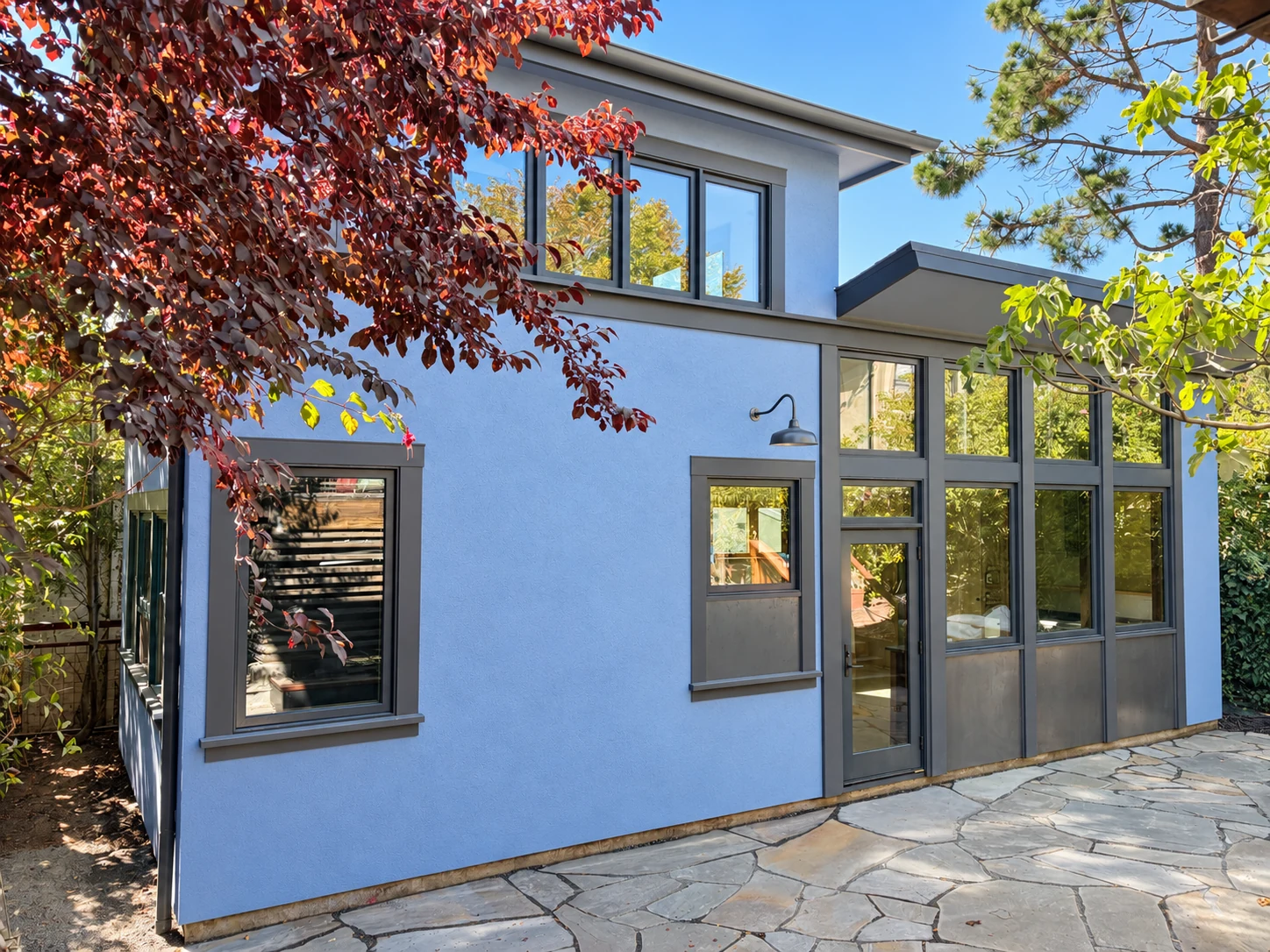 Blue stucco ADU with tall windows and a stone patio